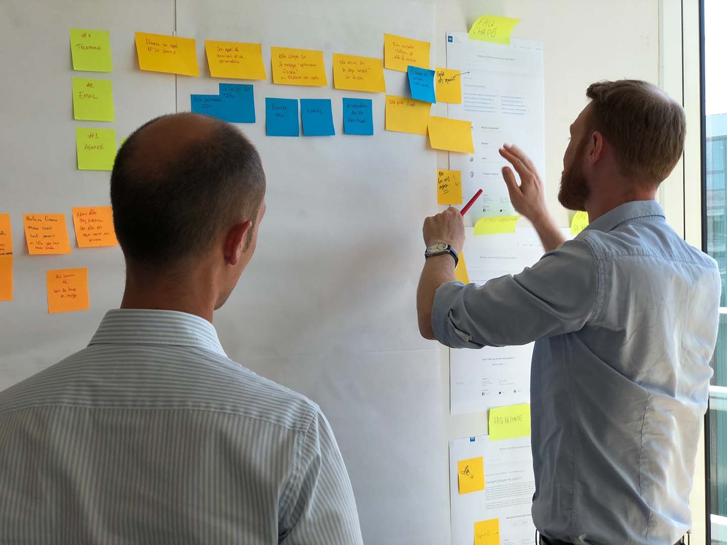 Two professionals reviewing user stories written on Post-It notes on a whiteboard