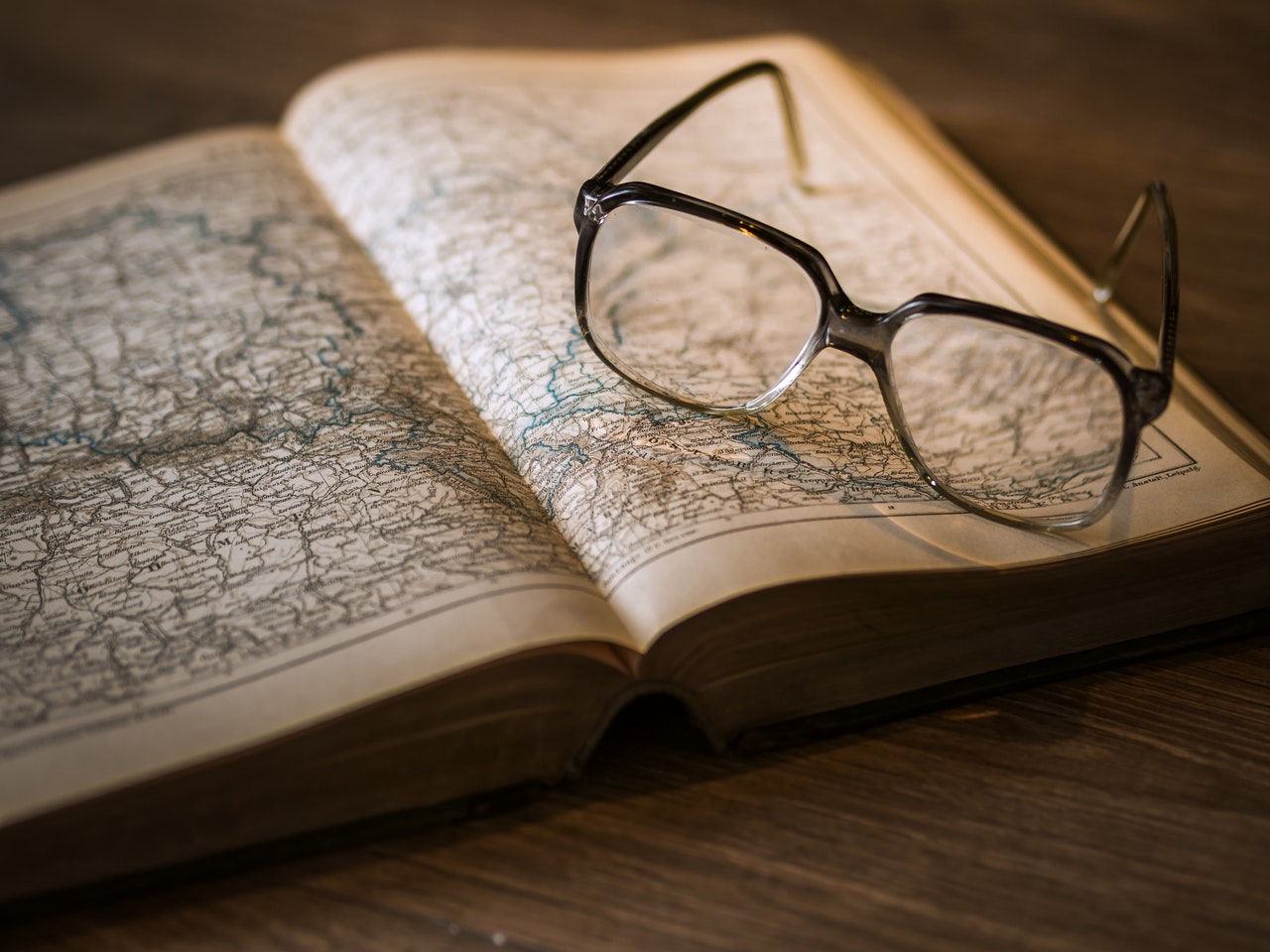 Book of maps sitting on table with pair of glasses on top of it