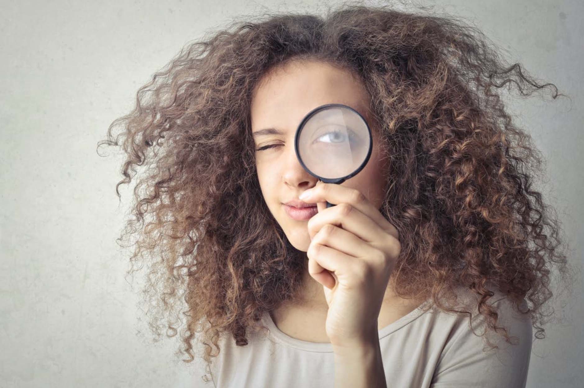 Young Black woman holding up magnifying glass to her left eye.