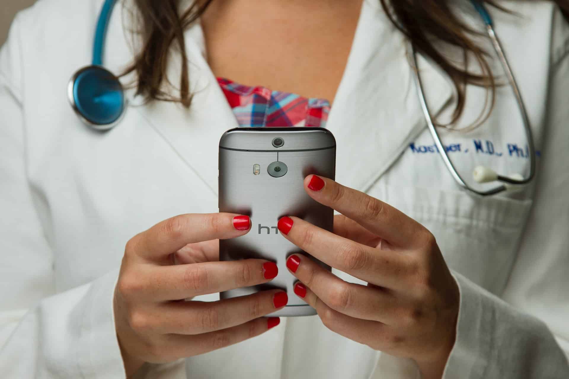 Female doctor with red painted nails holding a phone and enjoying modernized application