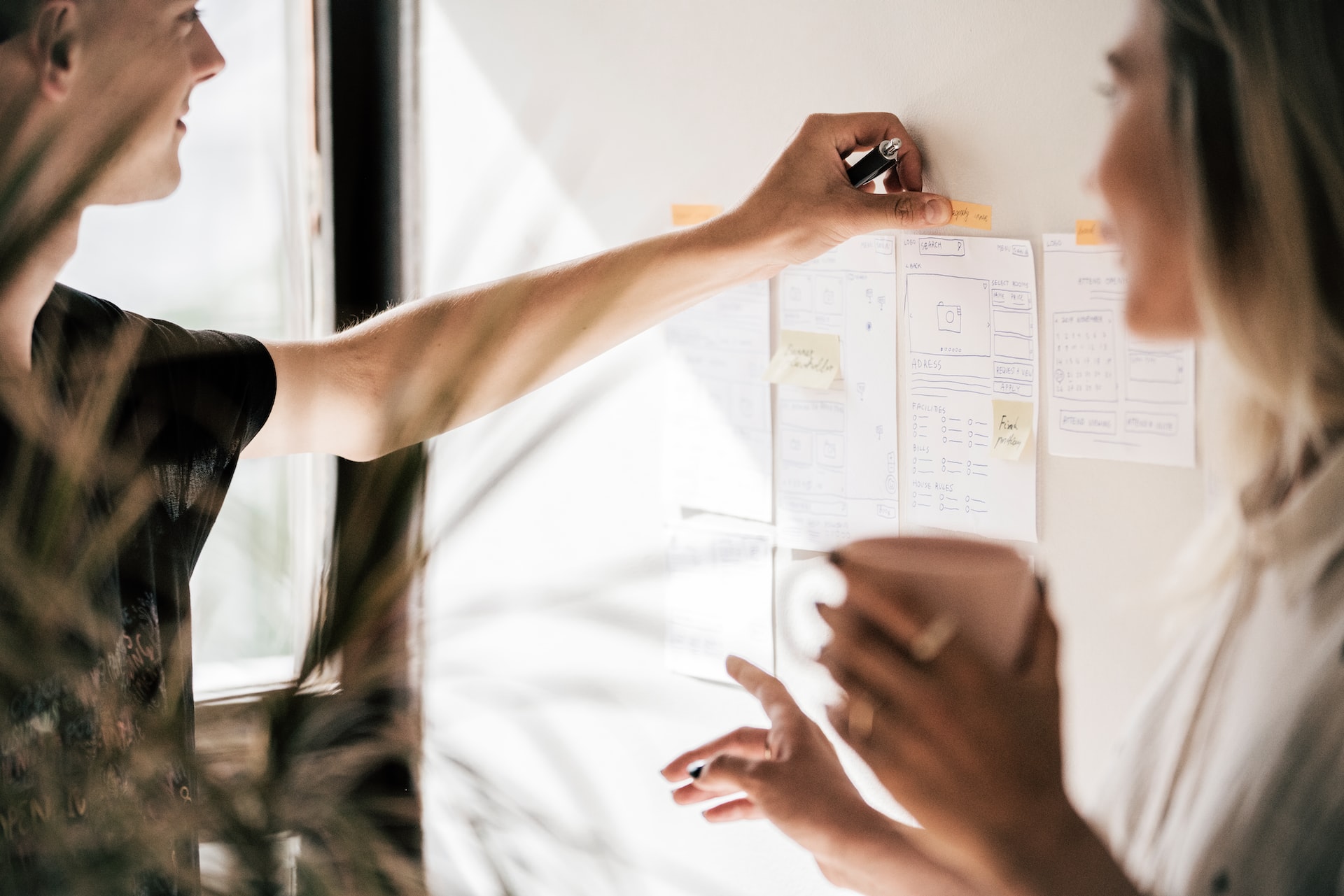 Two white professionals, one male and the other female, placing notes on wall outlining data goals