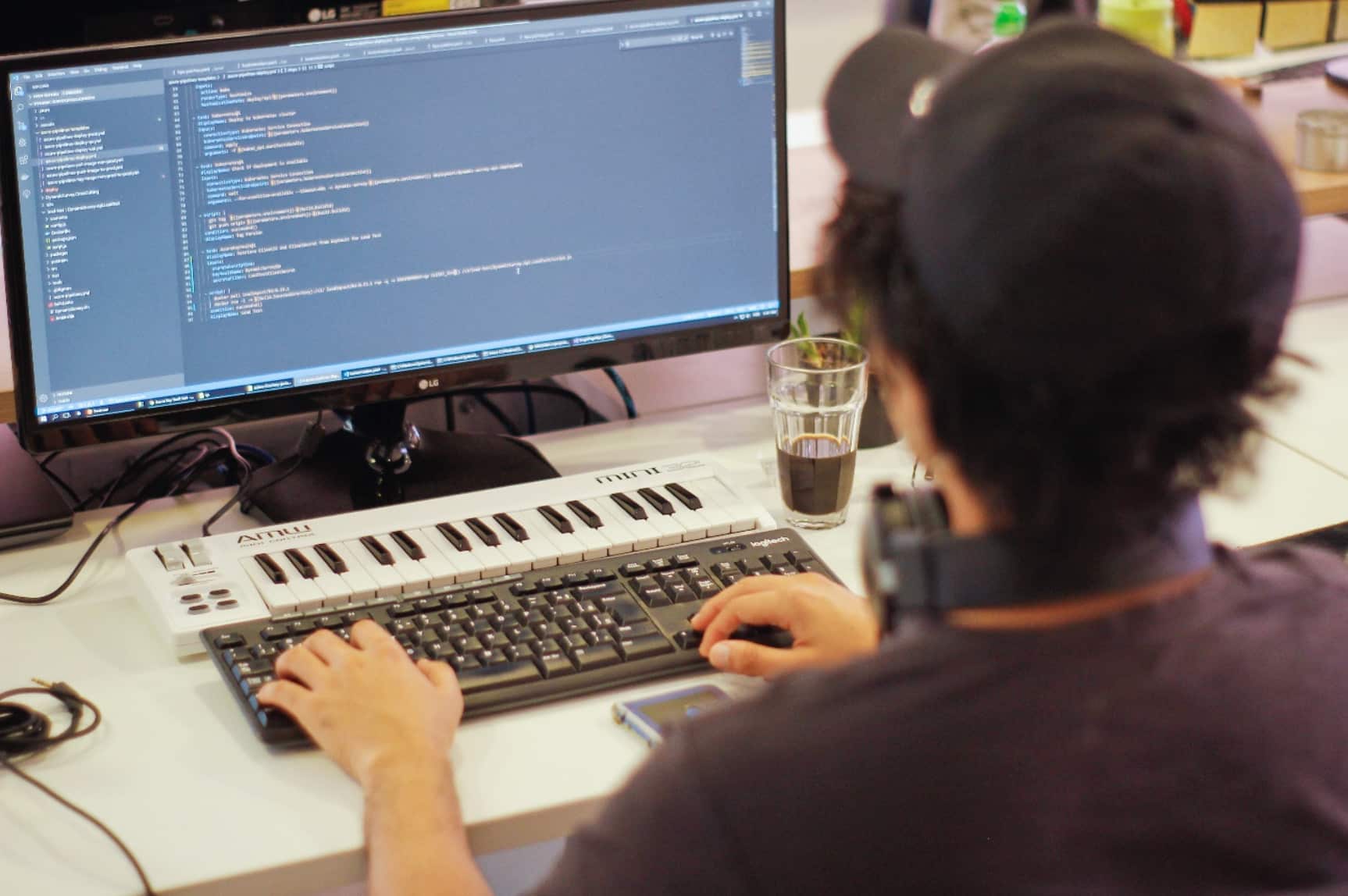 Young male professional with black baseball cap and cup of coffee coding as part of agile development