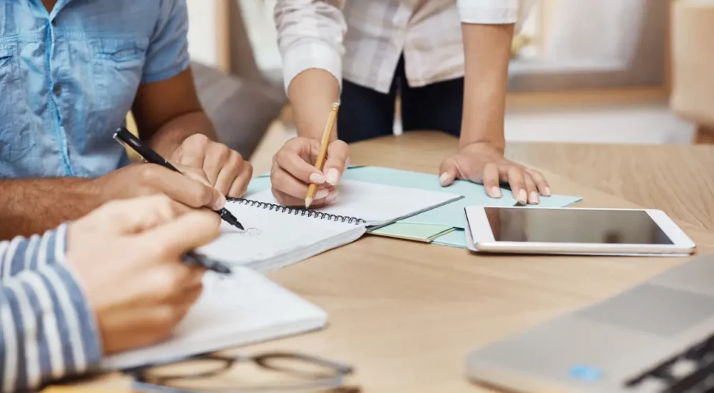 Three agile team members writing in notebooks while drafting next development sprint 
