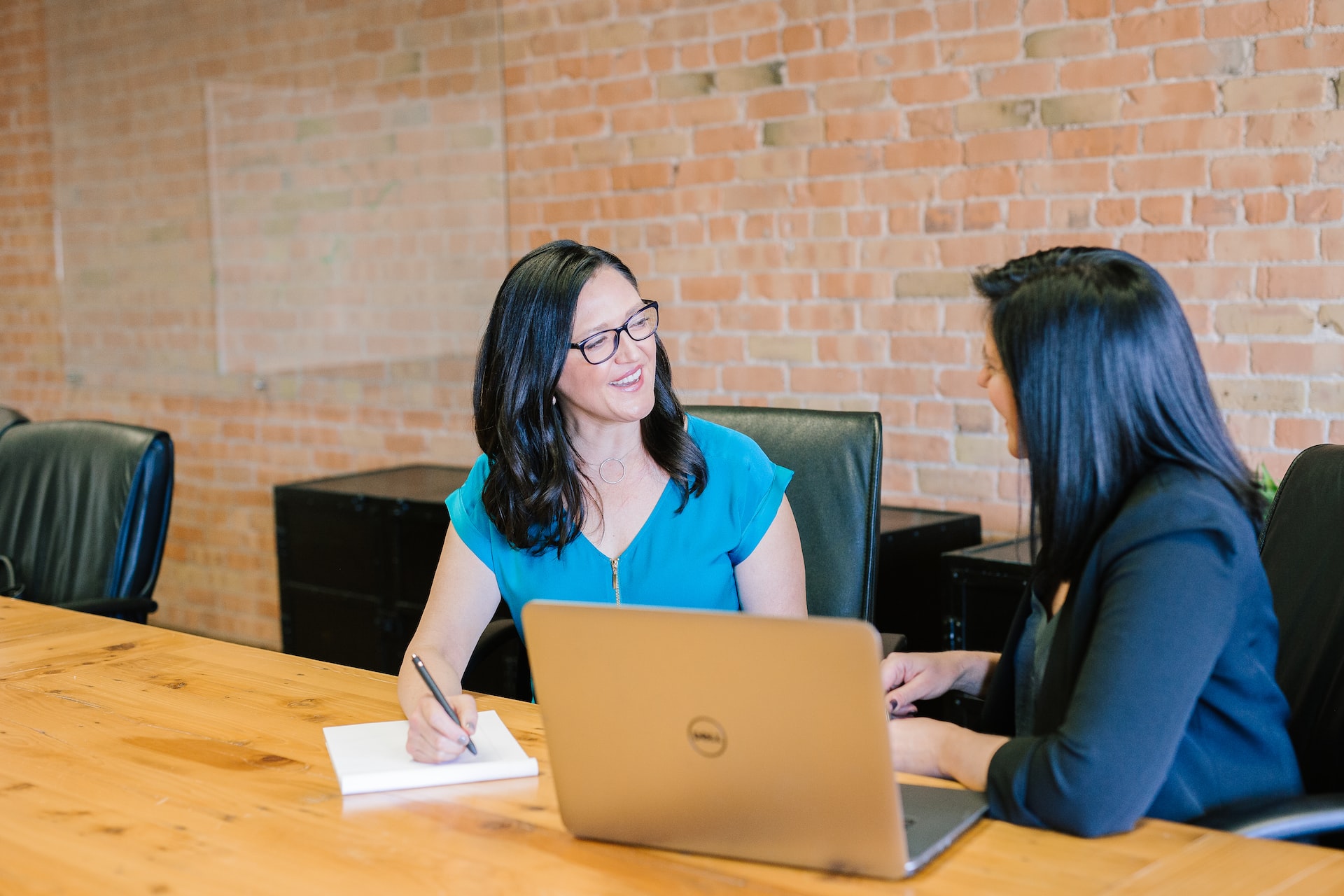 Two female employees collaborating at a table with laptop and notebook