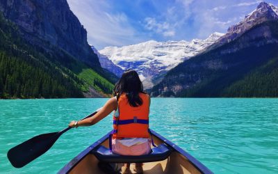 Woman rowing boat towards snow-capped mountains