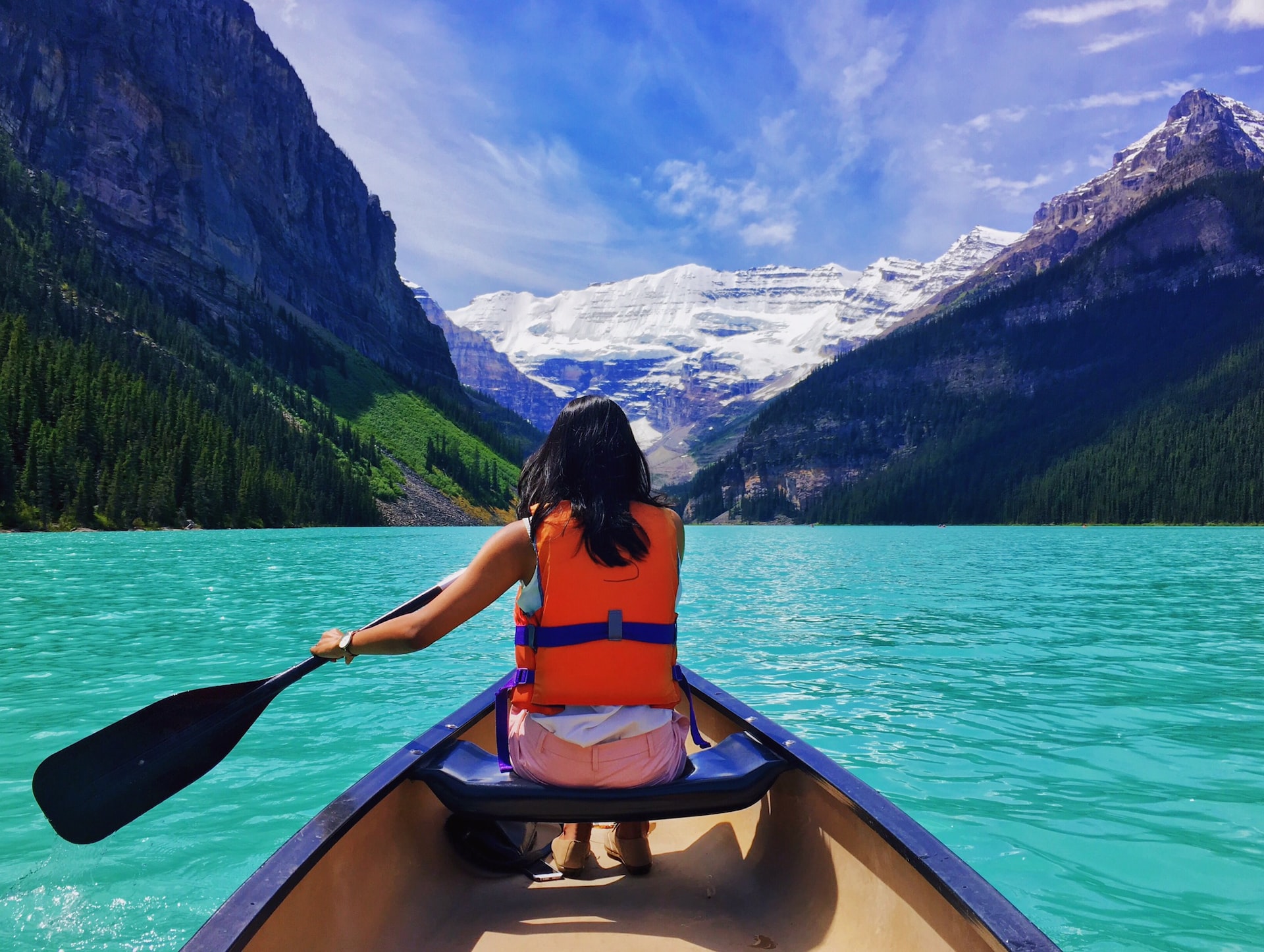 Woman rowing boat towards snow-capped mountains