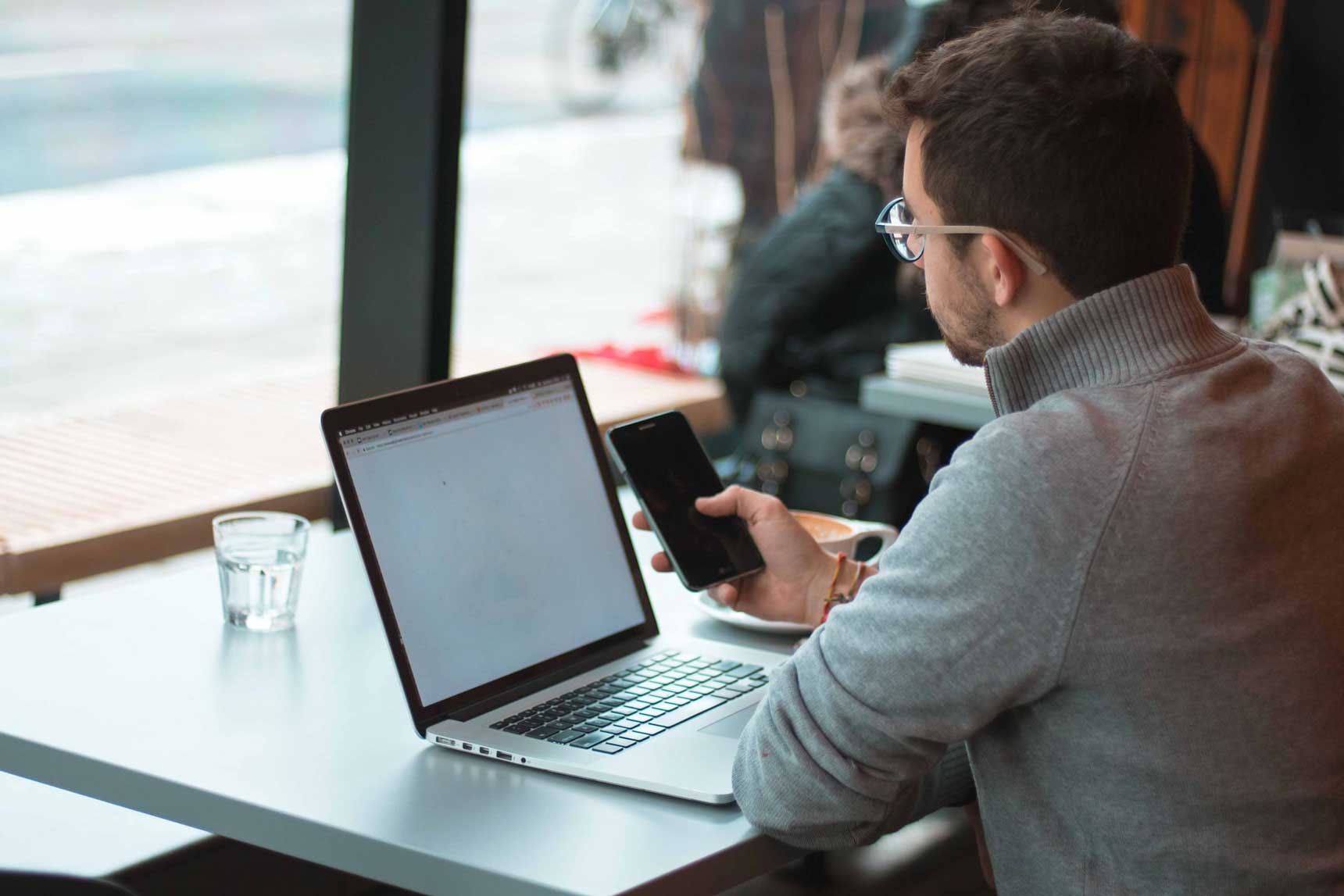 Man at a coffee shop using digital products on both his phone and laptop