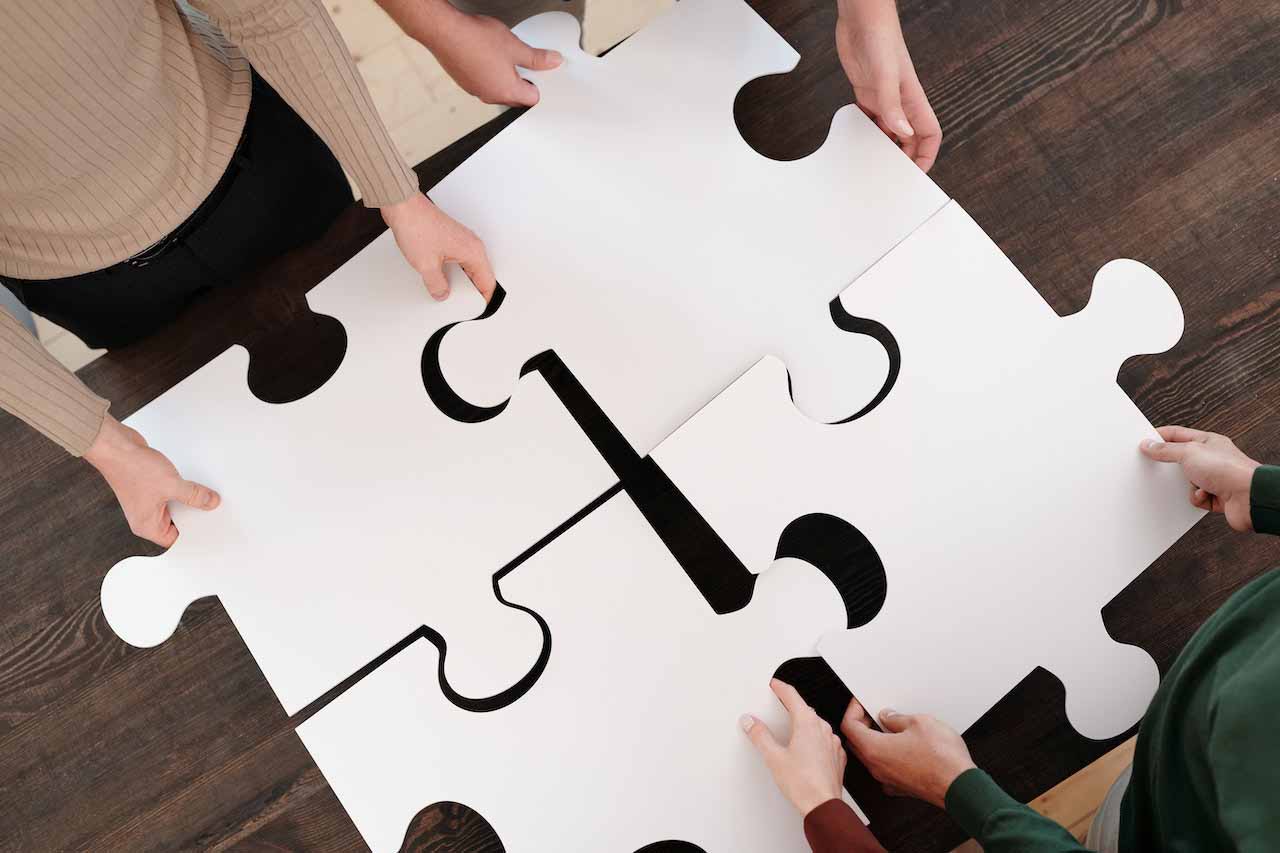 Four professionals putting together a puzzle at a work desk.