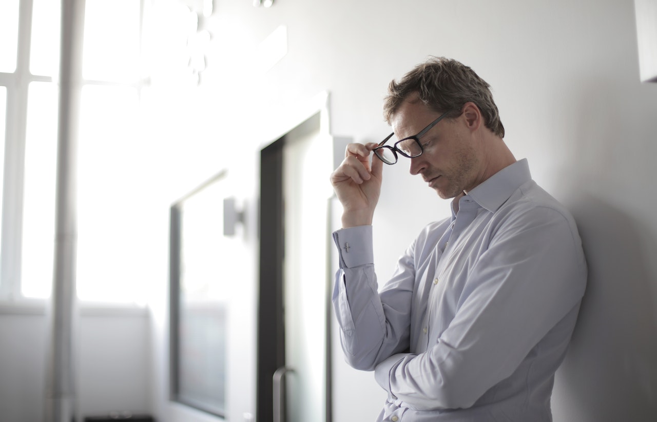 Executive standing against a white wall with glasses in hand, frustrated with progress of digital maturity