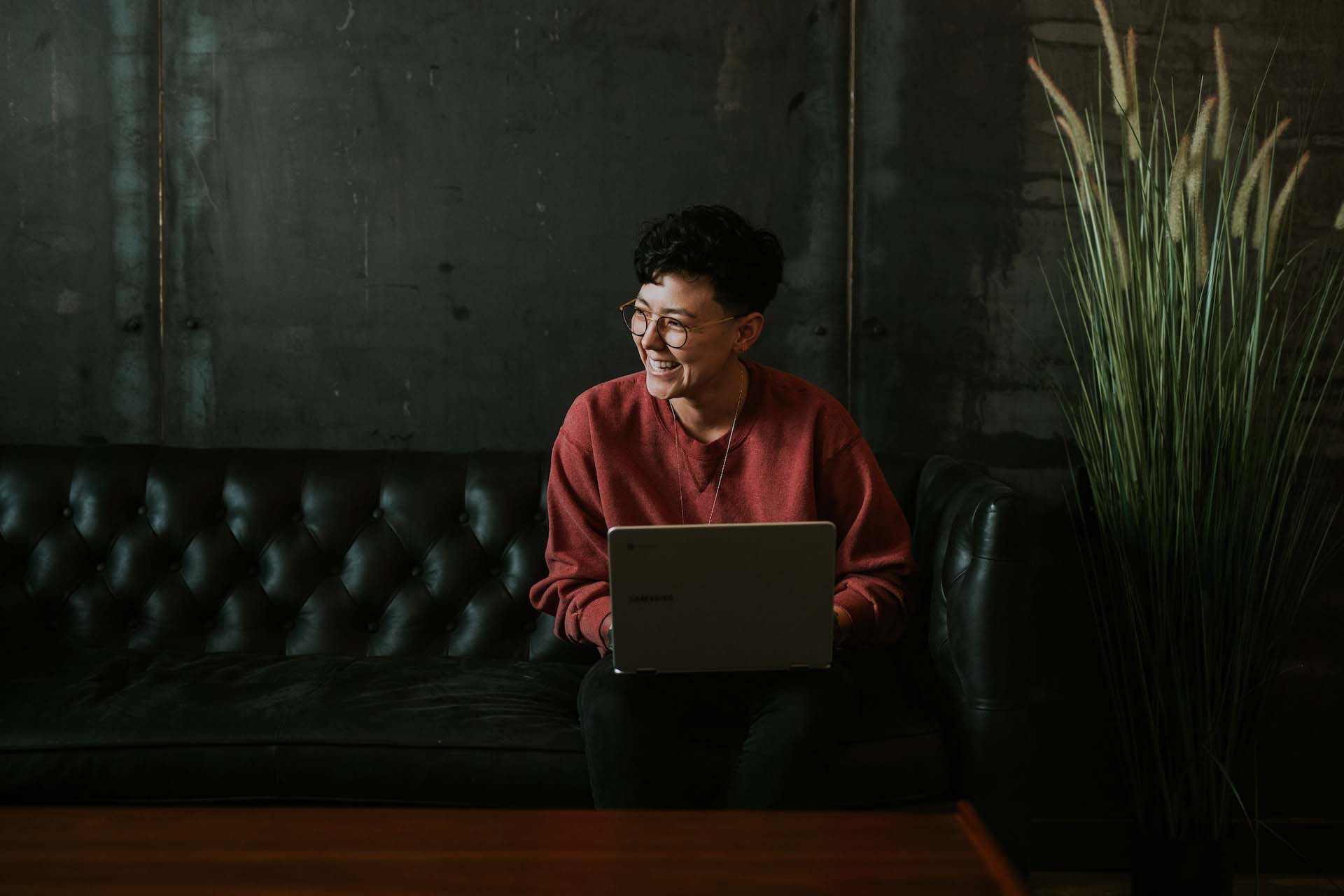 Young professional smiling on black couch with laptop after ChatGPT streamlined their work processes