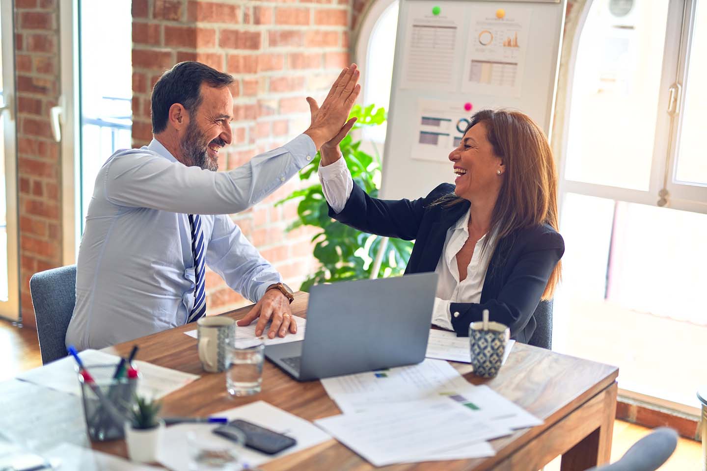 Two business executives high-fiving at desk after successful application modernization initiative