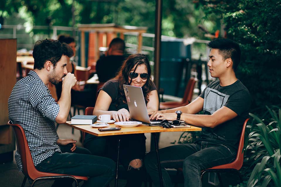 Three college students drinking coffee and navigating web application on a laptop together