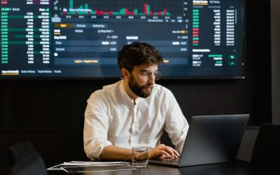 Man reviewing data on laptop with real-time data tracking display behind him