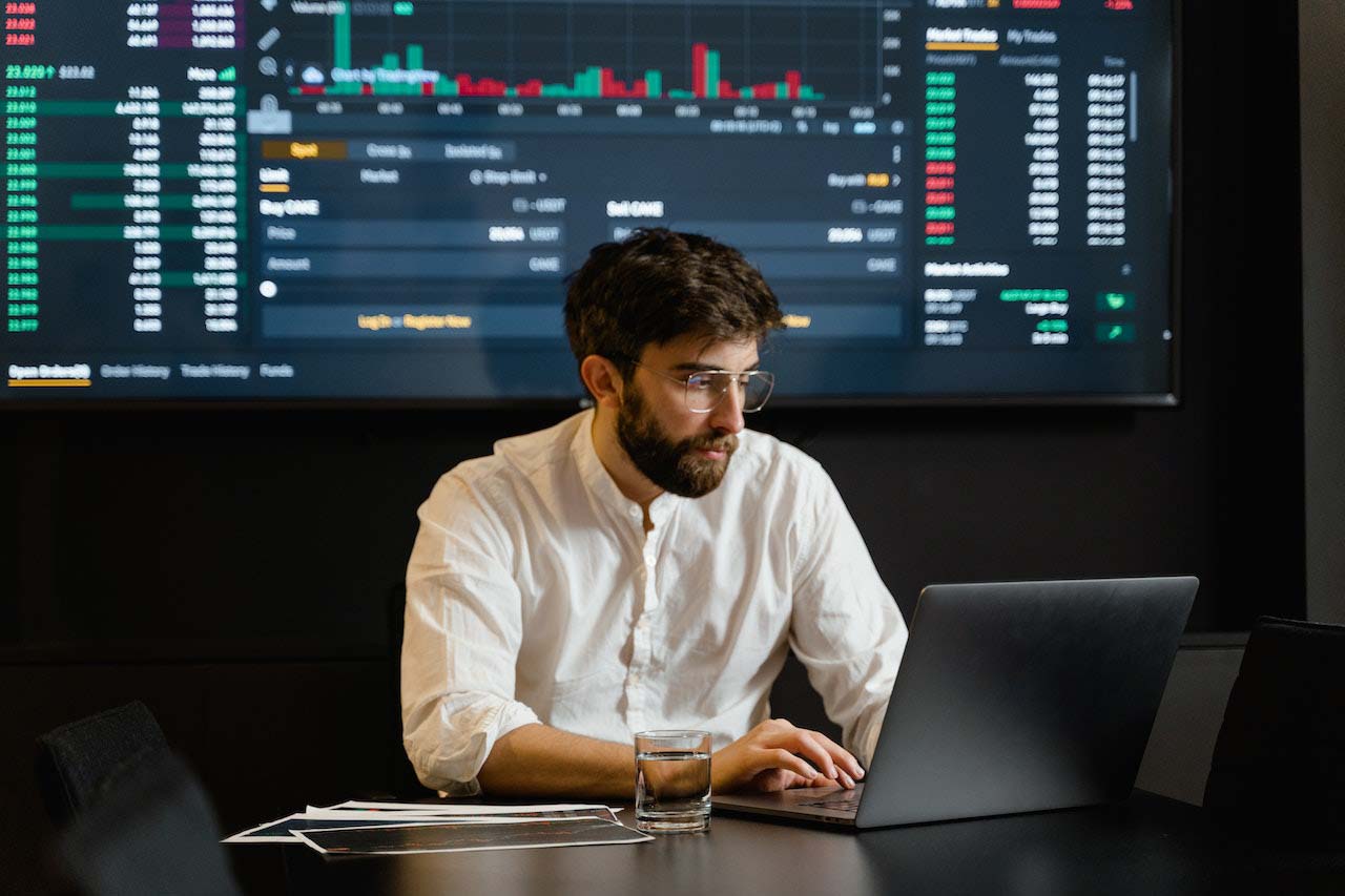 Man reviewing data on laptop with real-time data tracking display behind him