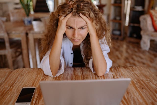 Woman at a table looking at her laptop, frustrated